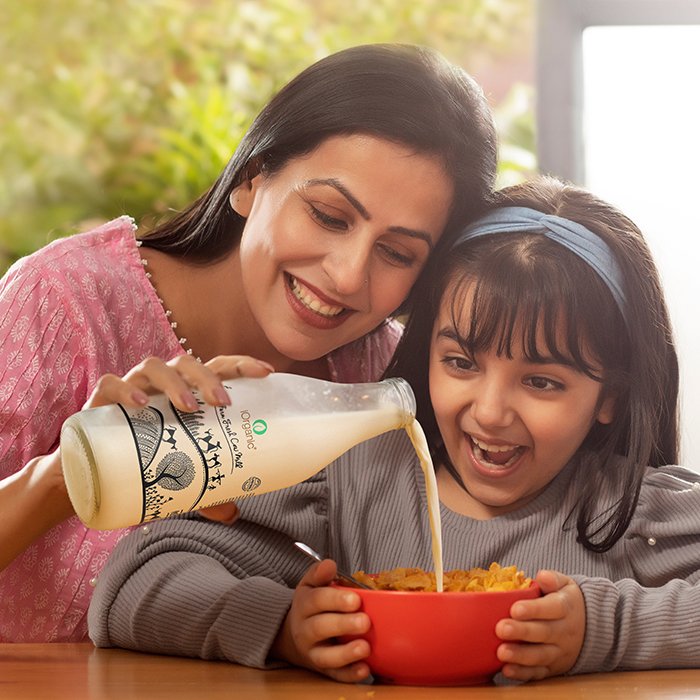 A HAPPY DAUGHTER LOOKS AT MILK BEING POURED ONTO CORNFLAKES BY MOTHER